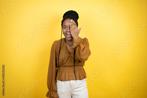 African american woman wearing casual clothes covering one eye with hand, confident smile on face and surprise emotion. © Irene