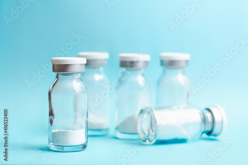 Glass vials with medicine in powder form on blue background, soft focus