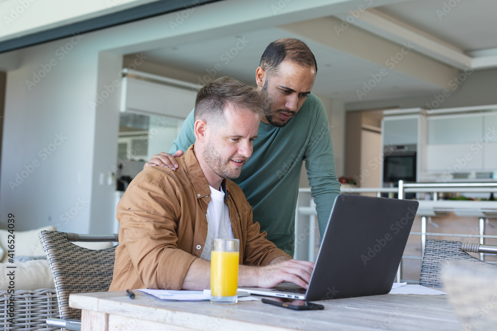 Multi ethnic gay male couple going through bills and using laptop at home Multi ethnic gay male couple going through bills and using laptop at home