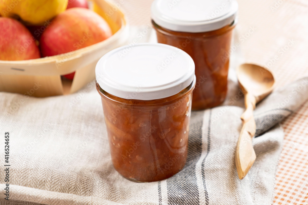 Homemade apple jam marmalade with cloves and cinnamon from organic apples in a transparent glass near wooden spoon. Homemade autumn jam confiture preserves. Homemade apple jam marmalade with cloves and cinnamon from organic apples in a transparent glass near wooden spoon. Homemade autumn jam confiture preserves.