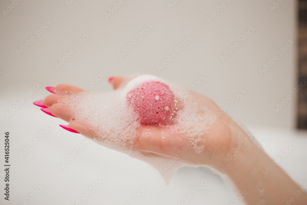 Female hand with a bright pink manicure holds a bath bomb in the foam Female hand with a bright pink manicure holds a bath bomb in the foam