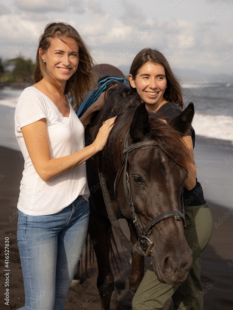 Obraz premium Two women hugging brown horse. Horse riding on the beach. Human and animals relationship. Nature concept. Copy space. Bali, Indonesia