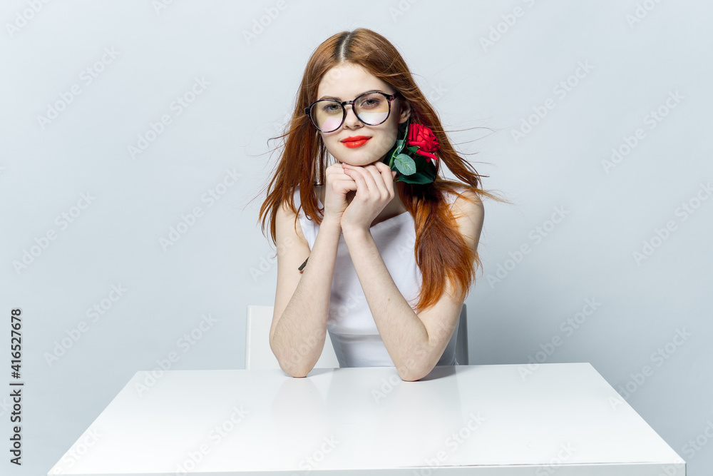 pretty red-haired woman sitting at the table with rose flower in her hands glamor red lips model pretty red-haired woman sitting at the table with rose flower in her hands glamor red lips model