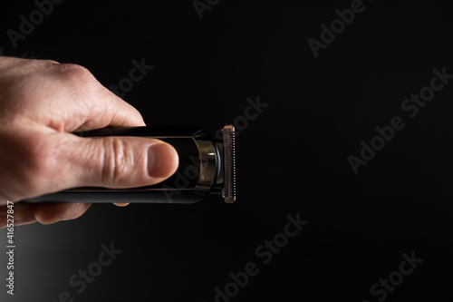 Hand with trimmer on black background.