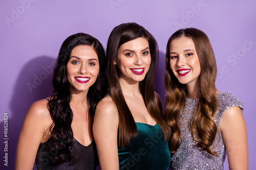 Photo of three cheerful ladies look camera shiny white smile wear dresses isolated purple color background