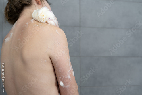 Close-up of woman with foam on skin using bath loofah while taking shower at home.