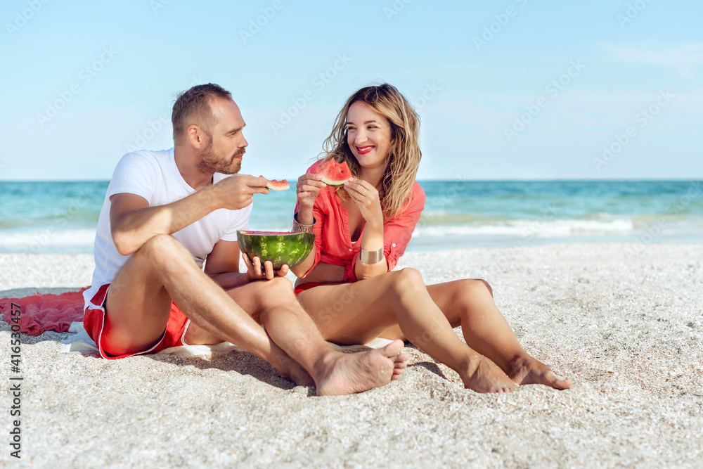 Young smiling couple eating watermelon on the beach having fun.