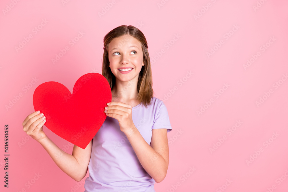 Photo of dreamy adorable little girl look empty space hold big red paper heart isolated on pink color background Photo of dreamy adorable little girl look empty space hold big red paper heart isolated on pink color background