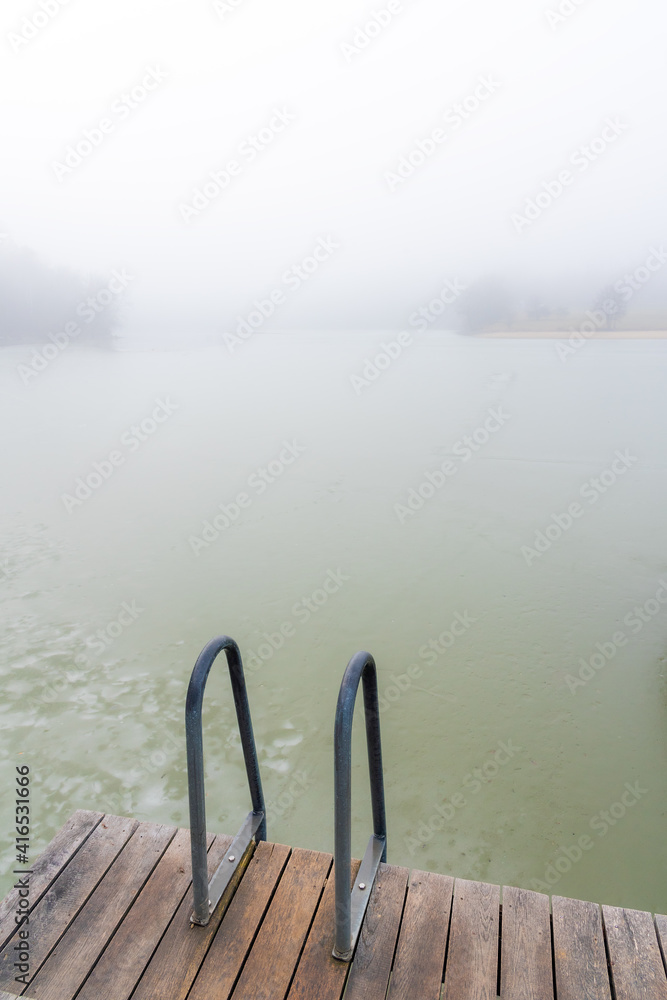 A pier and ladder on calm winter frozen lake. Winter sports, Hardening. 