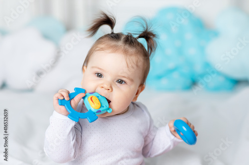 Obraz na plátne baby bites a rodent or toy with his teeth on the bed at home, teething