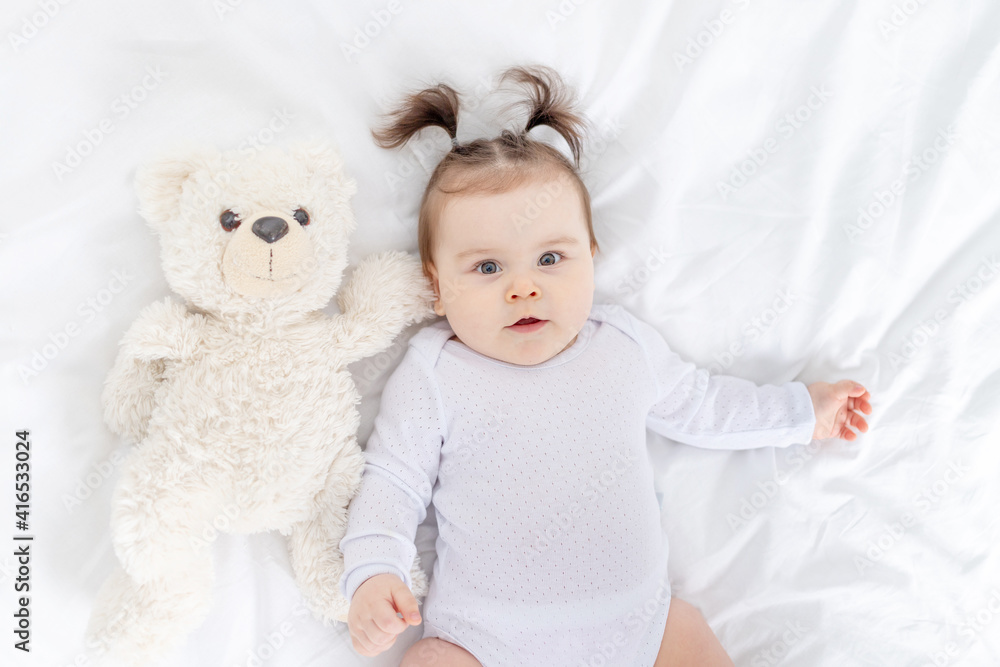 baby with a teddy bear lying on the bed at home, the concept of play and development of children