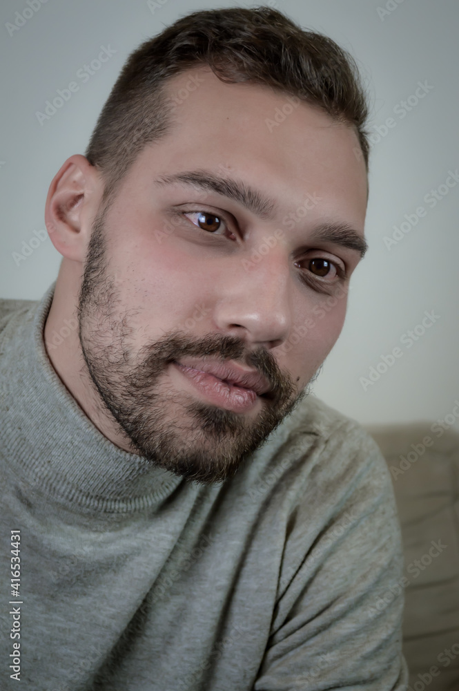 Fototapeta premium Portrait of a young brown-haired man with a short beard and a gray turtleneck sweater