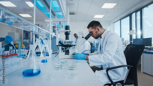 Modern Medical Research Laboratory: Male Scientist Working with Microscope, Analysing Biochemicals Samples. Advanced Scientific Lab for Medicine, Microbiology Development.