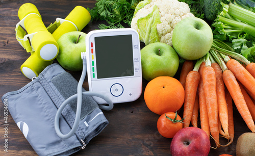 Blood pressure monitor and fresh fruits with vegetables against wooden table. Healthy lifestyle and prevention of hypertension concept
