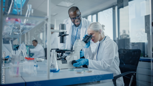 Modern Medical Research Laboratory  Two Scientists Working Together Using Microscope  Analysing Samples  Talking. Advanced Scientific Lab for Medicine  Biotechnology.