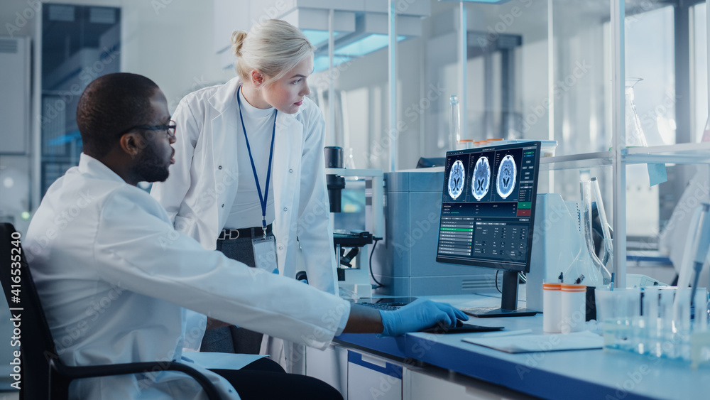 Modern Medical Research Laboratory: Two Scientists Use Computer with Screen Showing MRI Brain Scans, Specialists Discuss Innovative Technology. Advanced Scientific Lab for Medicine Modern Medical Research Laboratory: Two Scientists Use Computer with Screen Showing MRI Brain Scans, Specialists Discuss Innovative Technology. Advanced Scientific Lab for Medicine