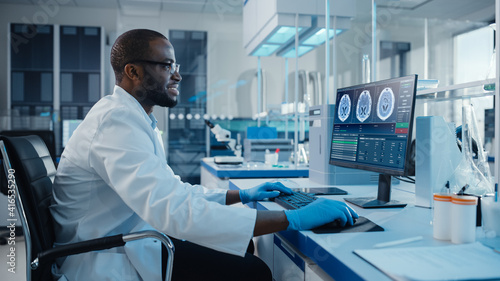 Modern Medical Laboratory: Male Scientist, Typing on Keyboard, Working on Computer, Scren Shows MRI Brain Scans. Advanced Scientific Lab, Medicine Technology Development.