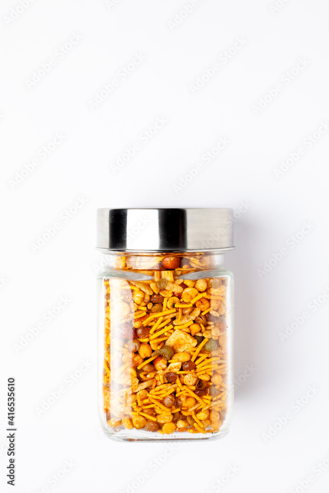 Hot spicy NavRatan snacks in a glass jar with a closed lid, made with red chili, peanuts, corn flakes. Indian spicy snacks (Namkeen), Top view, over the white background. Hot spicy NavRatan snacks in a glass jar with a closed lid, made with red chili, peanuts, corn flakes. Indian spicy snacks (Namkeen), Top view, over the white background.