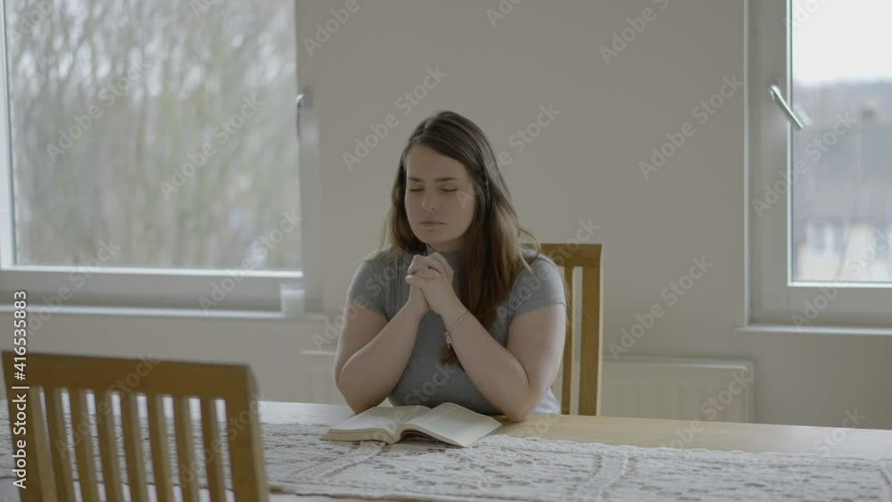 Woman praying alone seated by a wooden table at home Woman praying alone seated by a wooden table at home