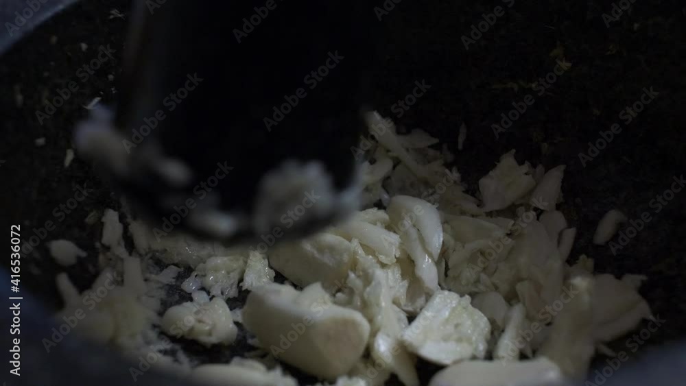 Close Up Of Garlic Cloves Being Crushed By Pestle In Stone Mortar. Locked Off Close Up Of Garlic Cloves Being Crushed By Pestle In Stone Mortar. Locked Off