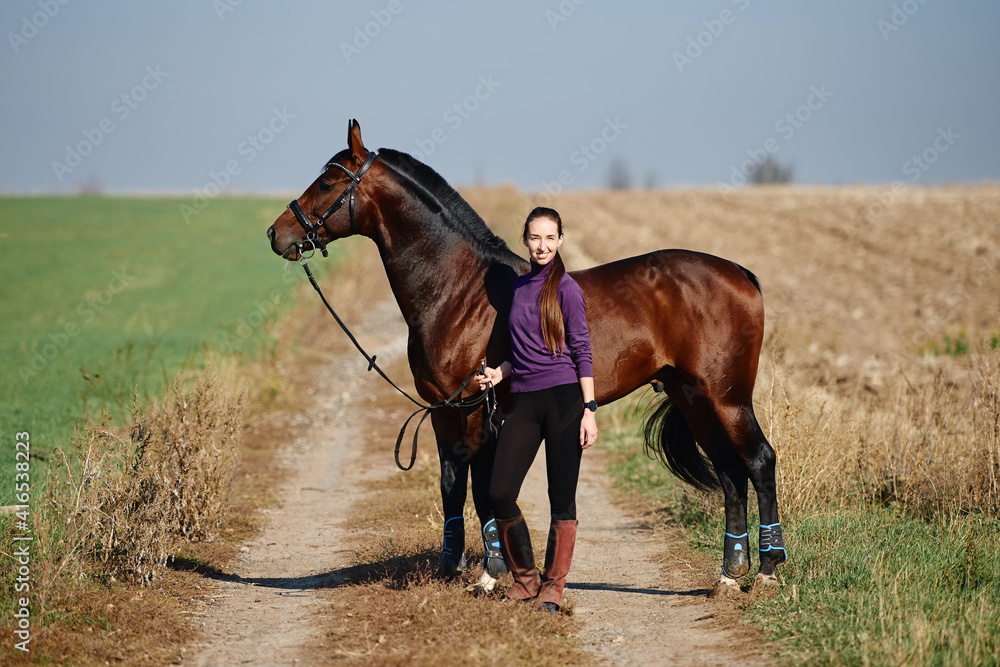 Young female farmer taking care about horse on ranch on summer day, copy space. Girl and brown horse outdoors