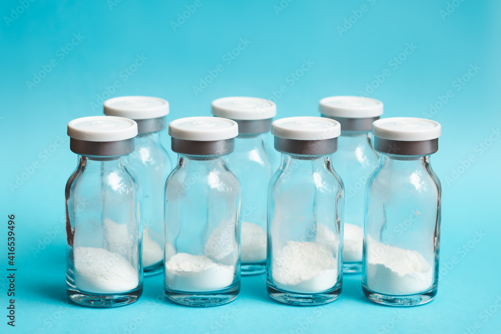 Glass vials of medicine in powder form lined up in a row on blue background, soft focus Glass vials of medicine in powder form lined up in a row on blue background, soft focus