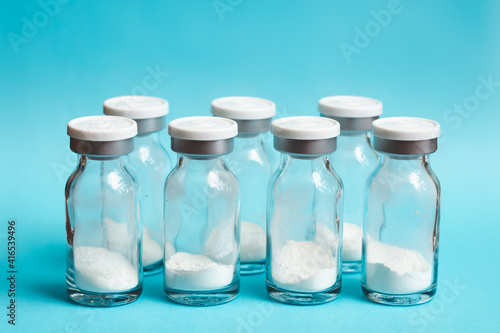 Glass vials of medicine in powder form lined up in a row on blue background, soft focus