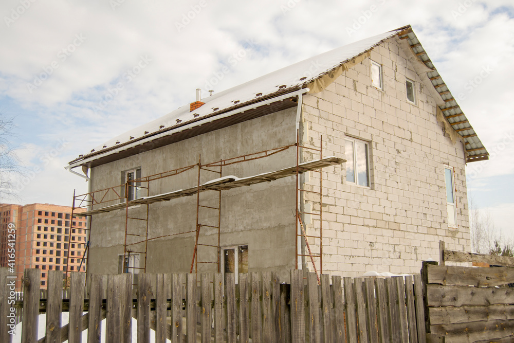 concrete house behind a wooden fence. snow covered earth. construction of a residential building in the background. scaffolding at a construction site. Construction in various forms concrete house behind a wooden fence. snow covered earth. construction of a residential building in the background. scaffolding at a construction site. Construction in various forms