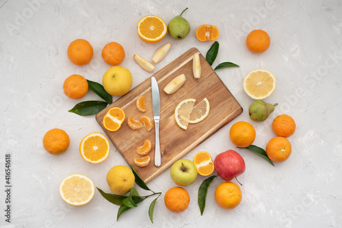 Many different fruits: tangerines, oranges, grapefruits, apples and pears with cutting board and knife on grey table. Fruits contain many vitamins, prepare fresh juices useful for healthy lifestyle. 