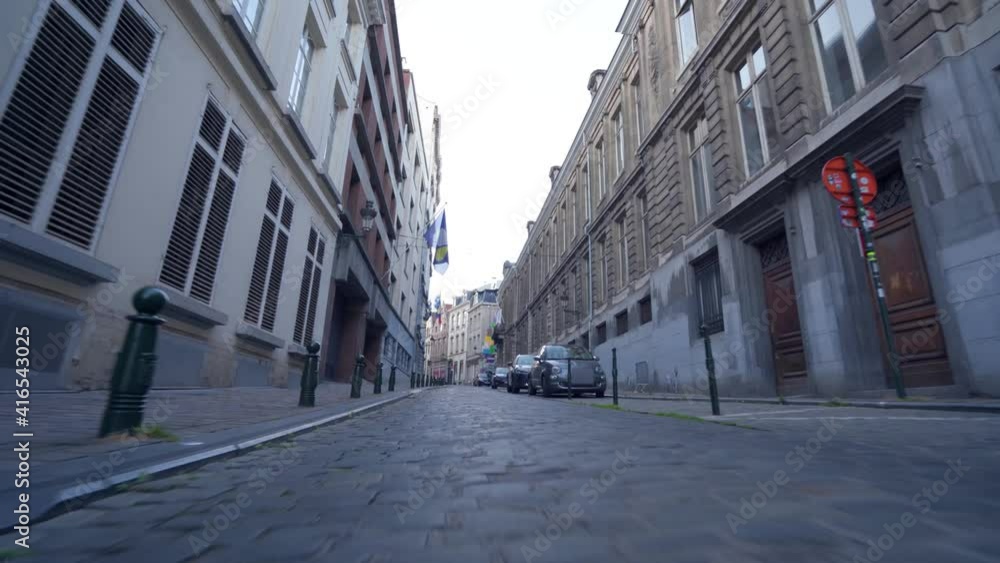 Low Forward Dolly shot over historic cobblestone road in city center of Brussels, Belgium, with streets parked in the car, Brussels flag hanging down the street. Low Forward Dolly shot over historic cobblestone road in city center of Brussels, Belgium, with streets parked in the car, Brussels flag hanging down the street.