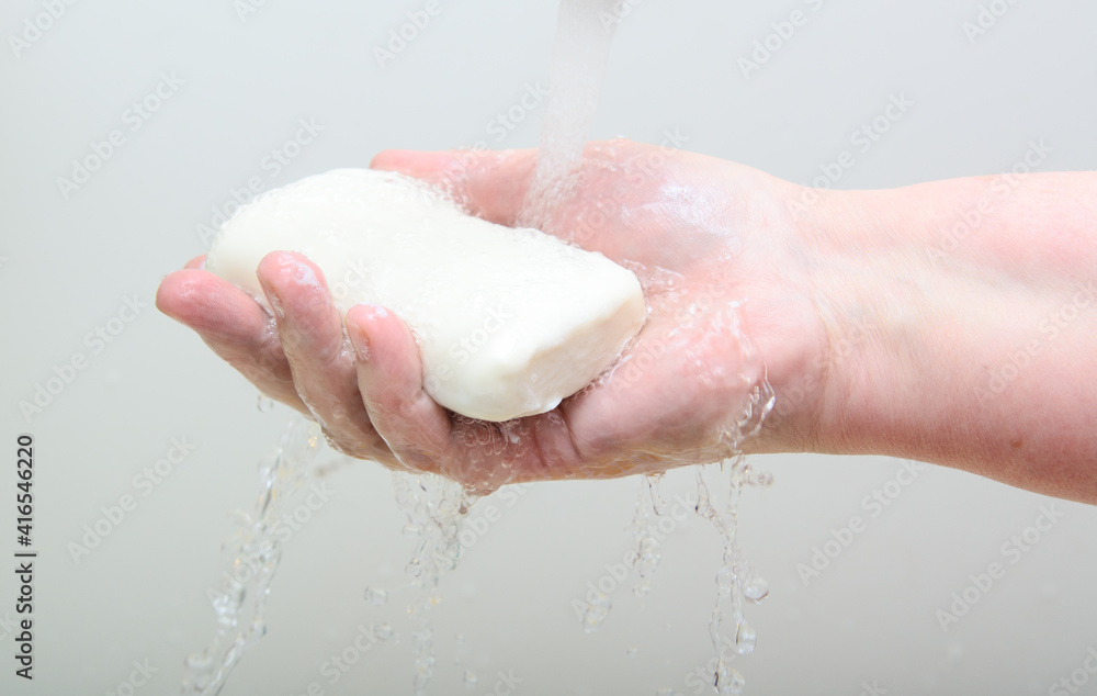 Fototapeta premium A bar of soap in a woman's hand. A stream of water from the tap pours on the hand. Concept-hygiene, quarantine
