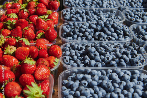 Plastic boxes with blueberries and strawberries at the market place on a sunny day. Farmers products.