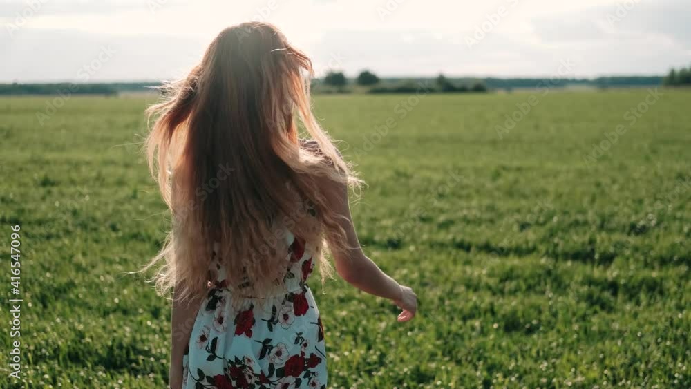A young girl happily walking in slow motion through green field. Beautiful carefree woman enjoying nature and sunlight. Joy, beauty in nature and environment concept. Freedom concept. A young girl happily walking in slow motion through green field. Beautiful carefree woman enjoying nature and sunlight. Joy, beauty in nature and environment concept. Freedom concept.