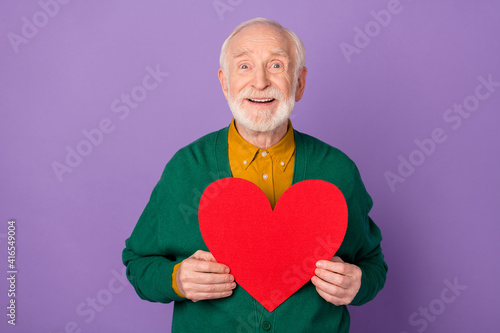 Photo of cheerful aged man hands hold big paper heart postcard toothy smile isolated on violet color background