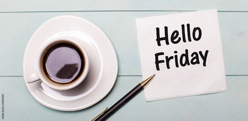 On a light blue wooden tray, there is a white cup of coffee, a handle and a napkin that says HELLO FRIDAY On a light blue wooden tray, there is a white cup of coffee, a handle and a napkin that says HELLO FRIDAY