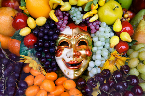 Smiling carnival mask surrounded by appetizing fruits. 