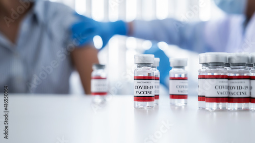 Covid-19 coronavirus vaccine bottles on white table with doctor injecting vaccine for middle aged woman background. Fight against Covid-19 coronavirus Concept.