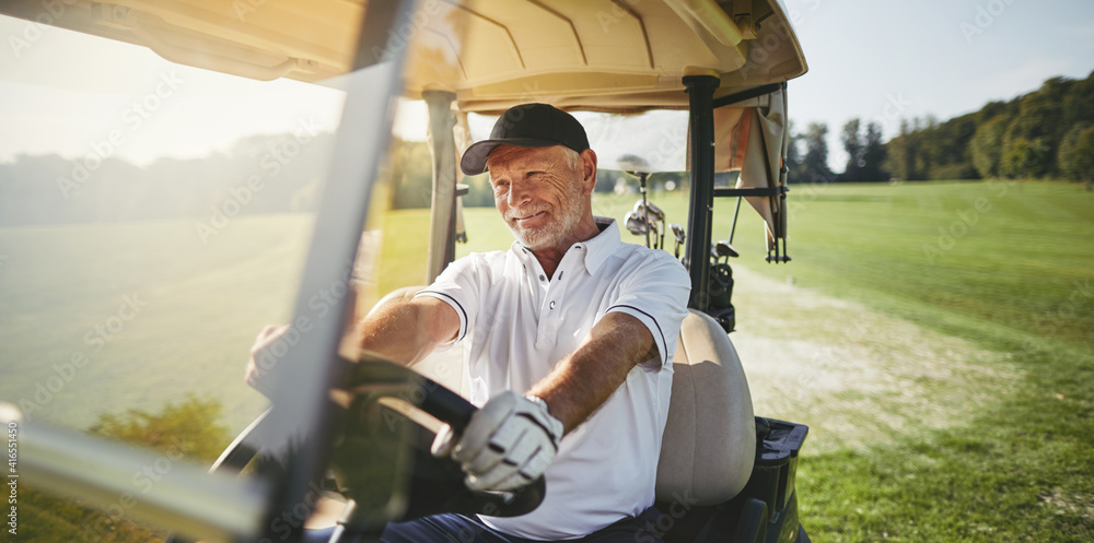 Fototapeta premium Smiling senior man driving his golf cart on a fairway