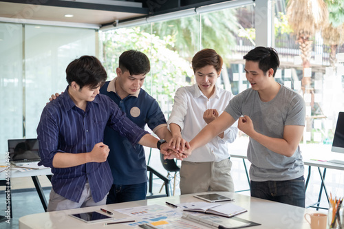 Group of young Asian man shaking hand in success together concept using a tablet and graph at the office.