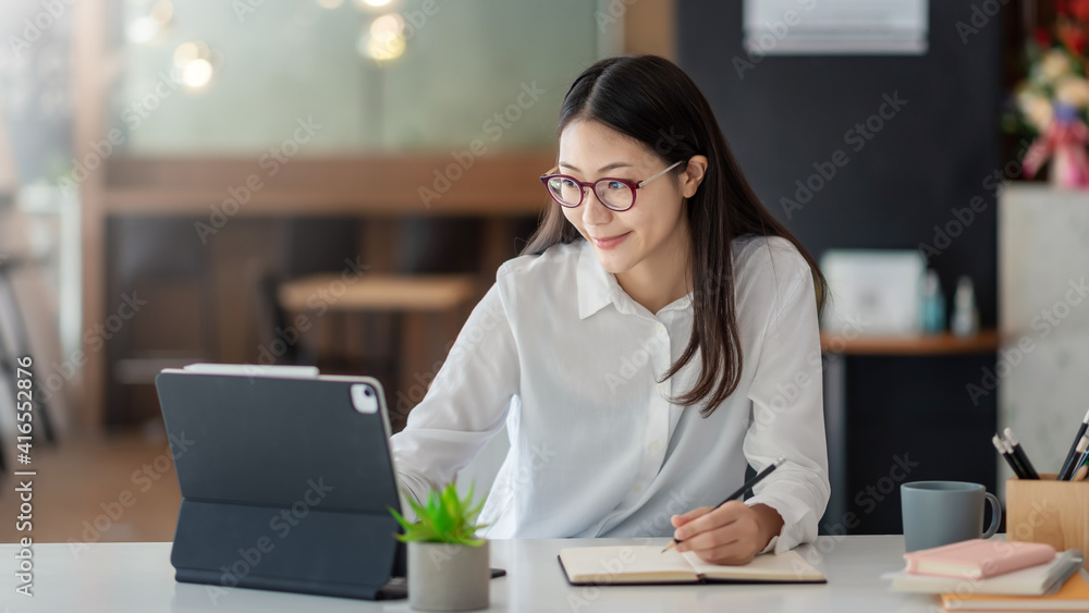 Young Asian woman working on a tablet and taking notes at the office. Young Asian woman working on a tablet and taking notes at the office.