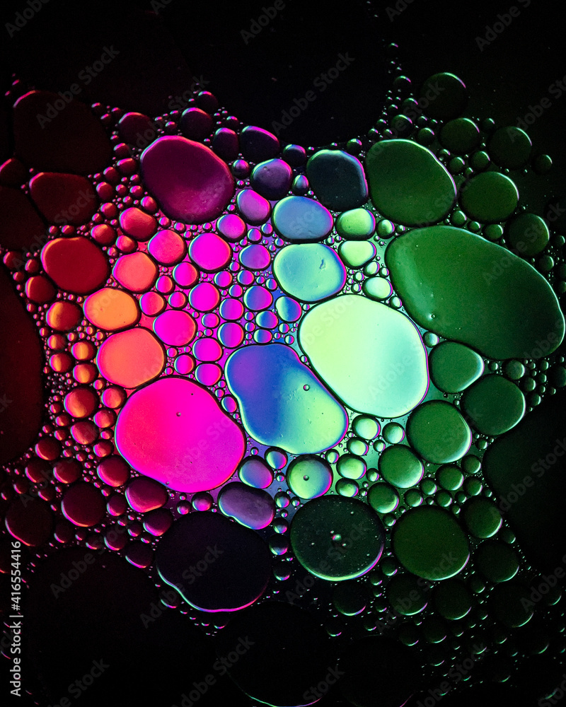 Oil drop bubbles on a water surface abstract with a green, blue and pink background