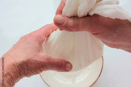 фотографія Old woman hands holding a homemade cottage cheese in cloth on white background