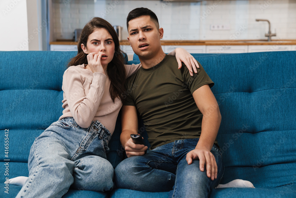 Obraz premium Photo of young scared couple watching tv