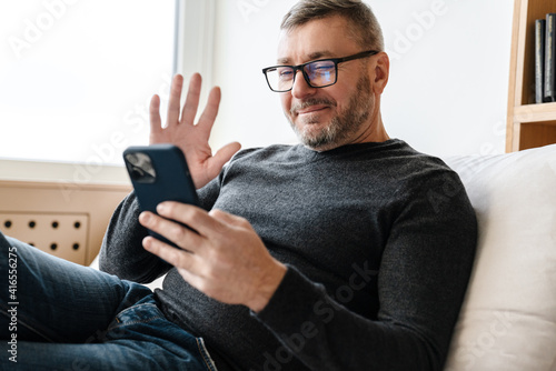 Happy adult unshaven man waving hand and using cellphone