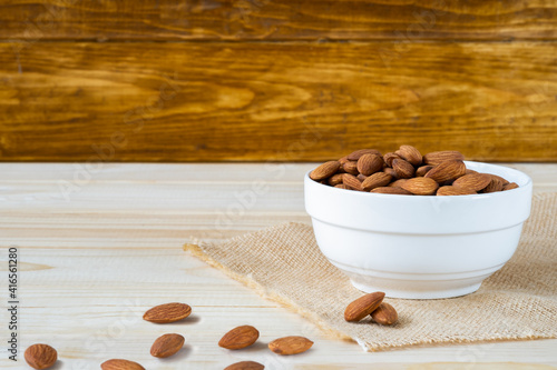 Almonds in white porcelain bowl on wooden table with wooden background and copy space for text.