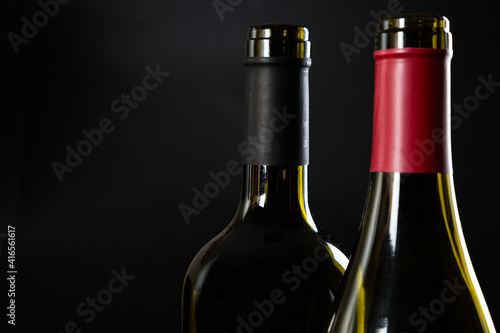 two open bottles of wine stand side by side on a dark glossy background.