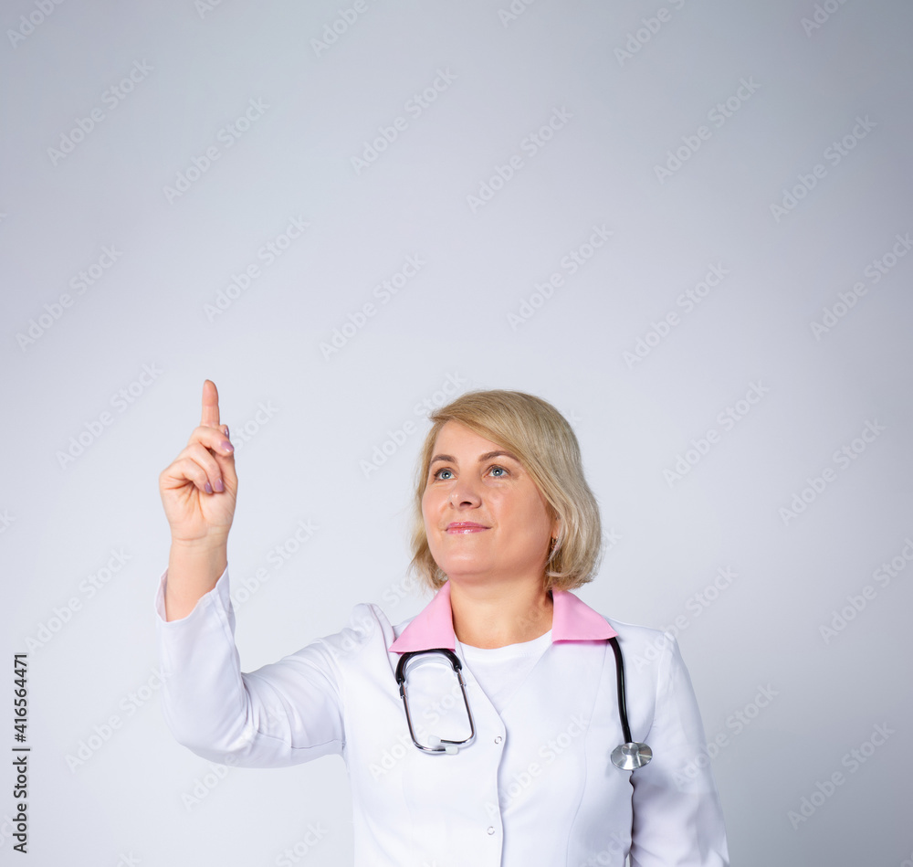 Excited doctor, blonde woman isolated on gray background. Female doctor in white medical gown point index finger up. Healthcare,personnel health, medicine. Copy space advertisement blank Excited doctor, blonde woman isolated on gray background. Female doctor in white medical gown point index finger up. Healthcare,personnel health, medicine. Copy space advertisement blank