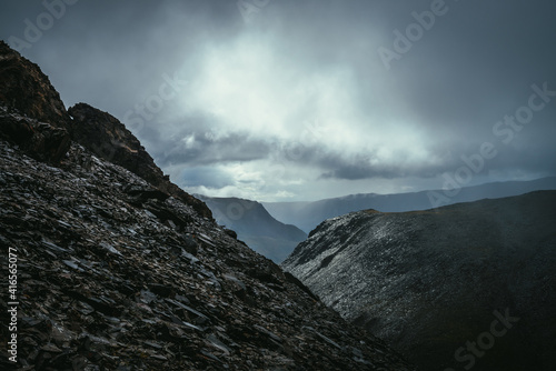 Dark atmospheric landscape on edge of abyss in highlands. Dangerous mountains and abyss in overcast weather. Danger mountain pass and sharp rocks under gray sky. Dangerous rainy weather in mountains.