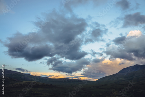 Beautiful mountain scenery with golden dawn light in cloudy sky. Scenic mountain landscape with illuminating color in sunset sky. Silhouettes of mountains on sunrise. Gold illuminating sunlight in sky