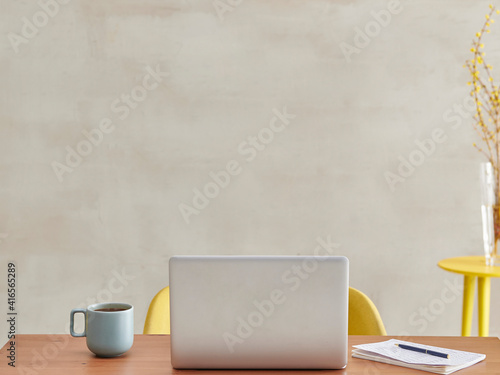 The back of laptop in the room, wooden table yellow chair coffee style.